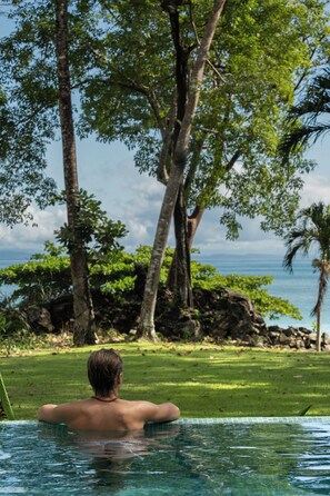A person relaxing in a swimming pool with a view of the ocean and trees. - Beachfront Solar Villa - Private Pool - Surf at Your Door - Osa Peninsula (Puntarenas Province)