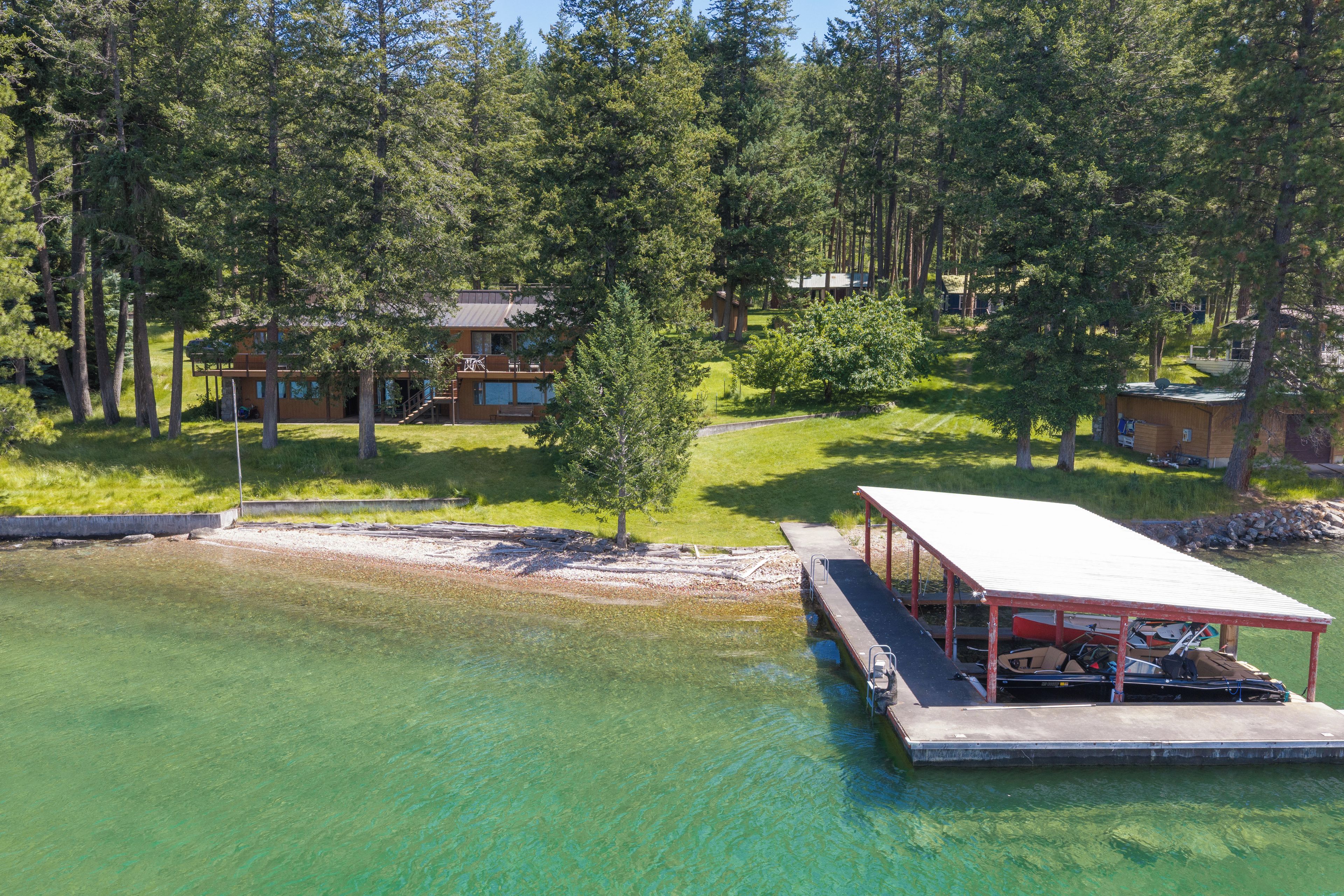 A lakeside property with a dock, a covered boat house, and a cabin surrounded by dense forest.