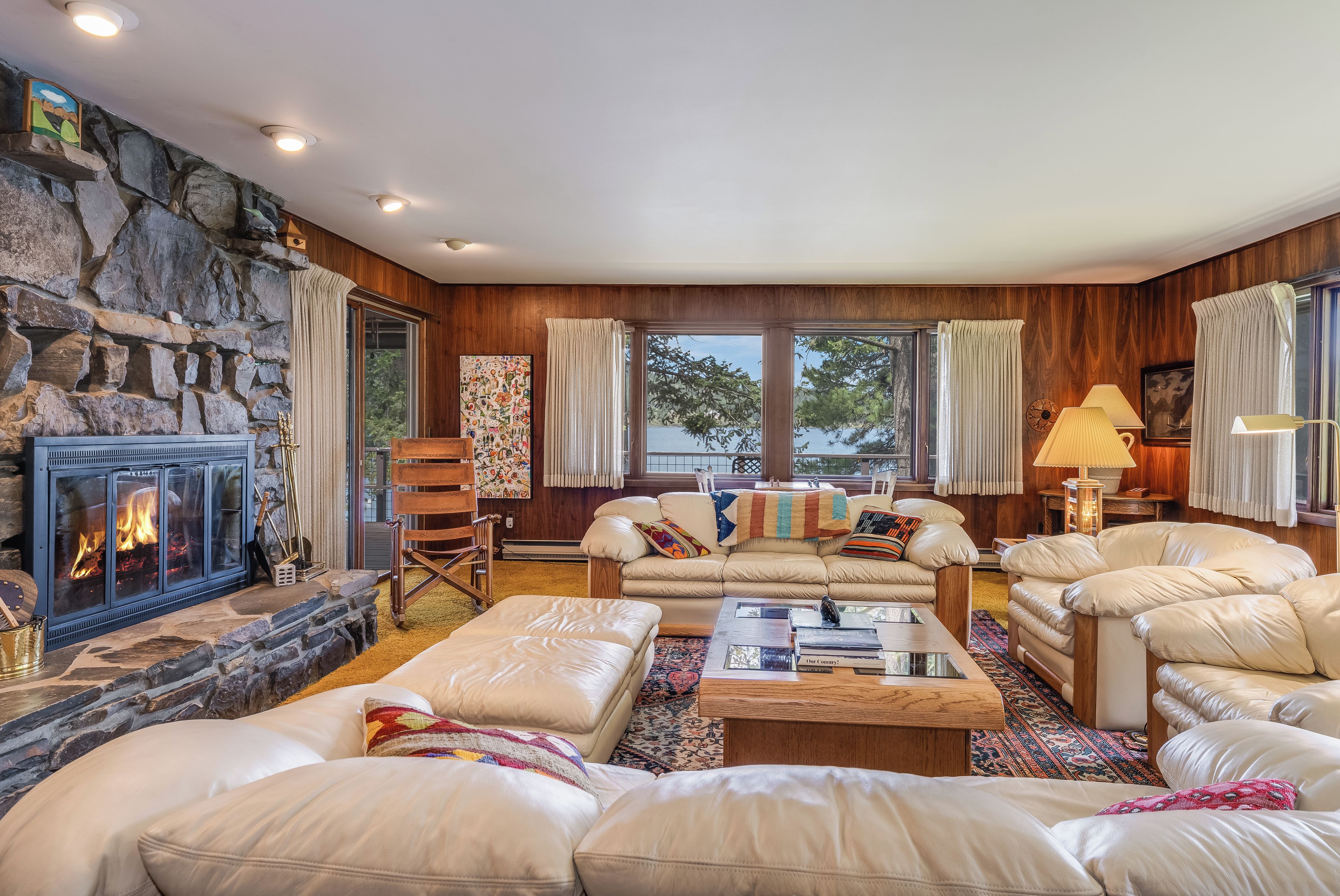A cozy living room with a stone fireplace, leather sofas, and a large window with curtains.
