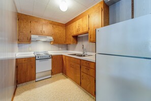 Une cuisine de taille réduite, dotée de meubles en bois, d’un réfrigérateur blanc, d’une cuisinière et d’un évier.