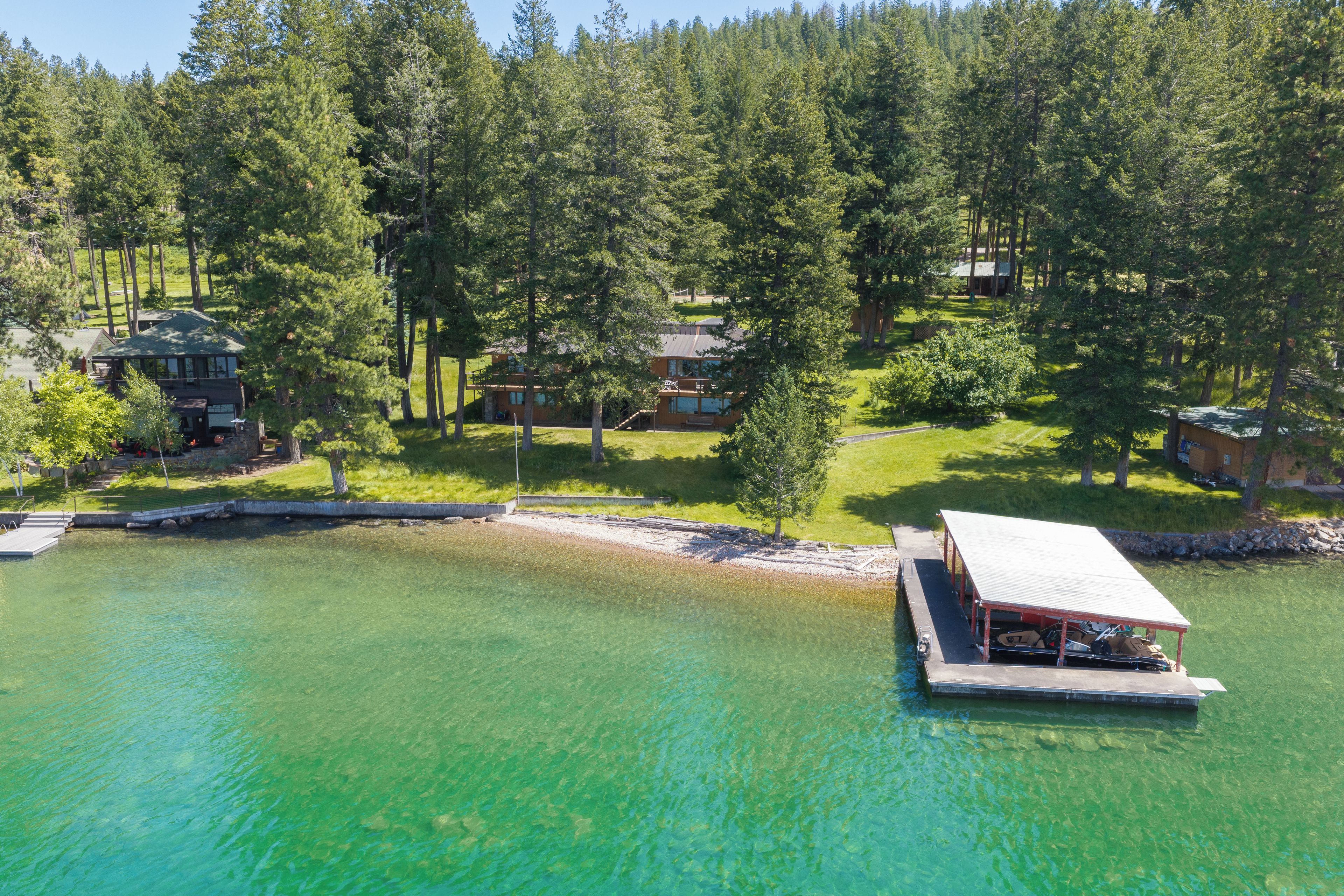 A lakeside property with a dock, clear water, and multiple cabins surrounded by dense forest.