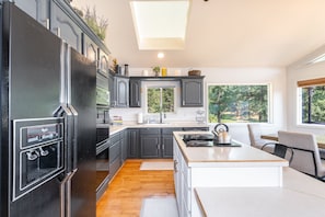 A modern kitchen with a central island, dark cabinetry, and a large window offering a view of trees. - New! Secluded 9.5-Acre Mountain Retreat with Jewel Basin Views, Near Flathead Lake (Bigfork)
