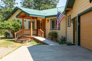 A two-story house with a porch, a flag, and a garage. - New! Secluded 9.5-Acre Mountain Retreat with Jewel Basin Views, Near Flathead Lake (Bigfork)