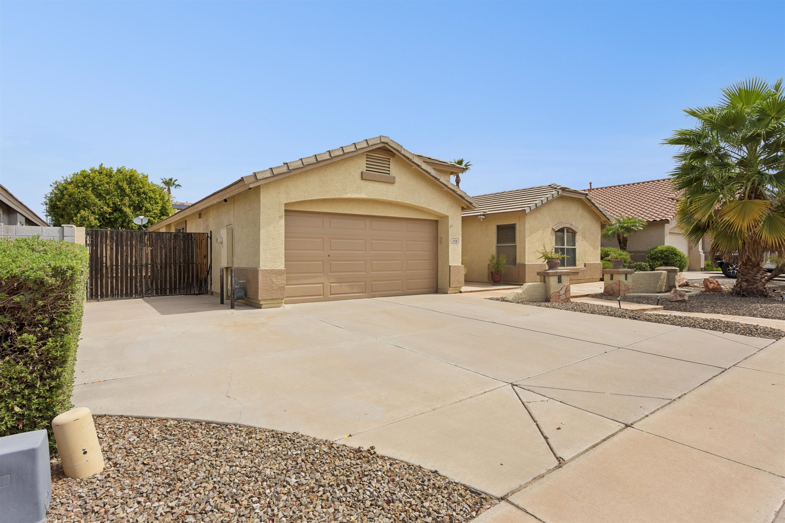 A residential garage with a brown door, a driveway leading to the garage, and a gated entrance.
