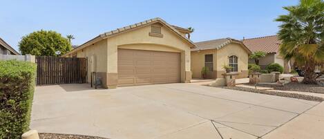A residential garage with a brown door, a driveway leading to the garage, and a gated entrance.