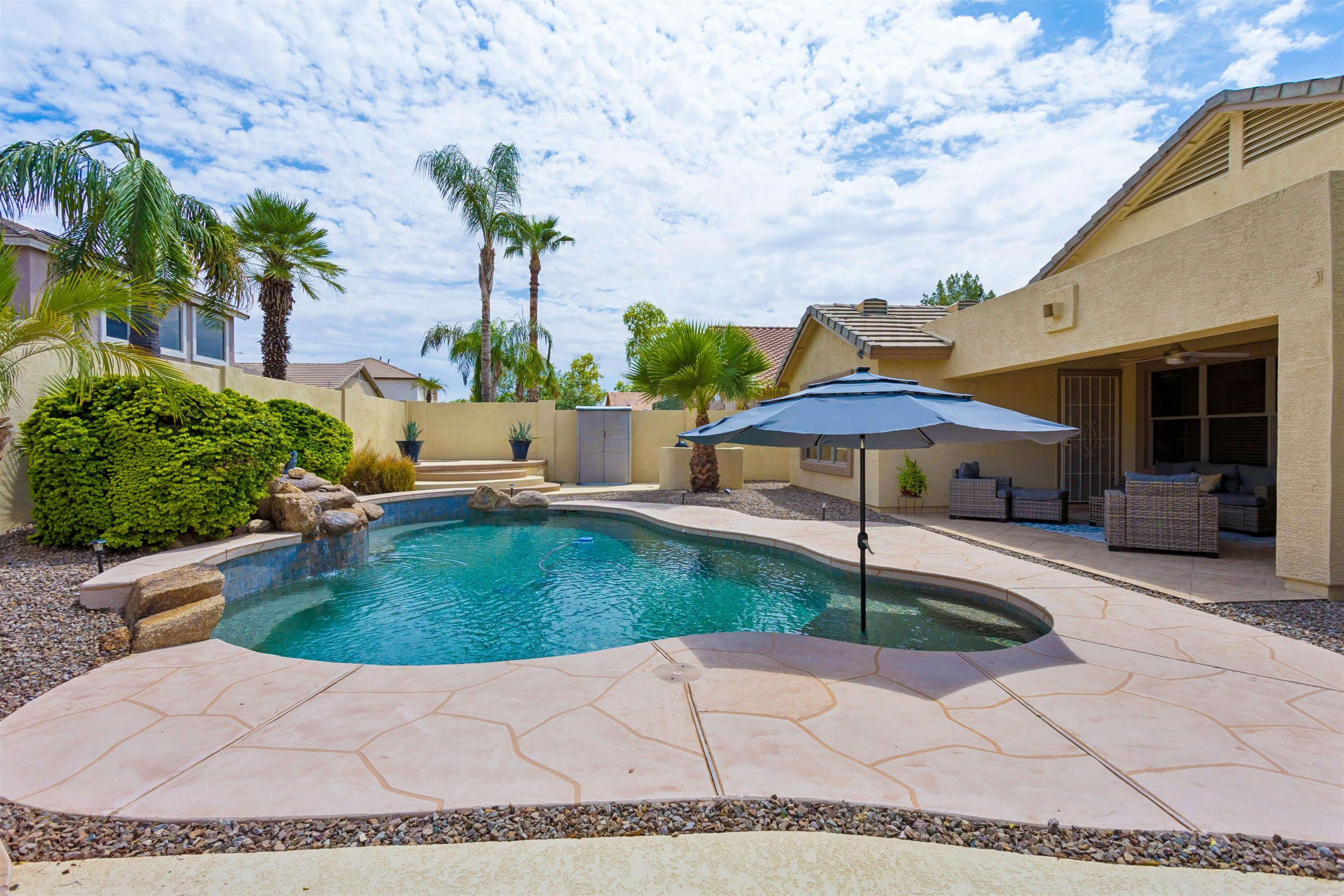 A backyard with a swimming pool, patio furniture, and a covered seating area.