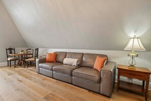 Ein Zimmer mit einem braunen Ledersofa, einem Holznachttisch mit Lampe und einem Essbereich mit Stühlen und Tisch.