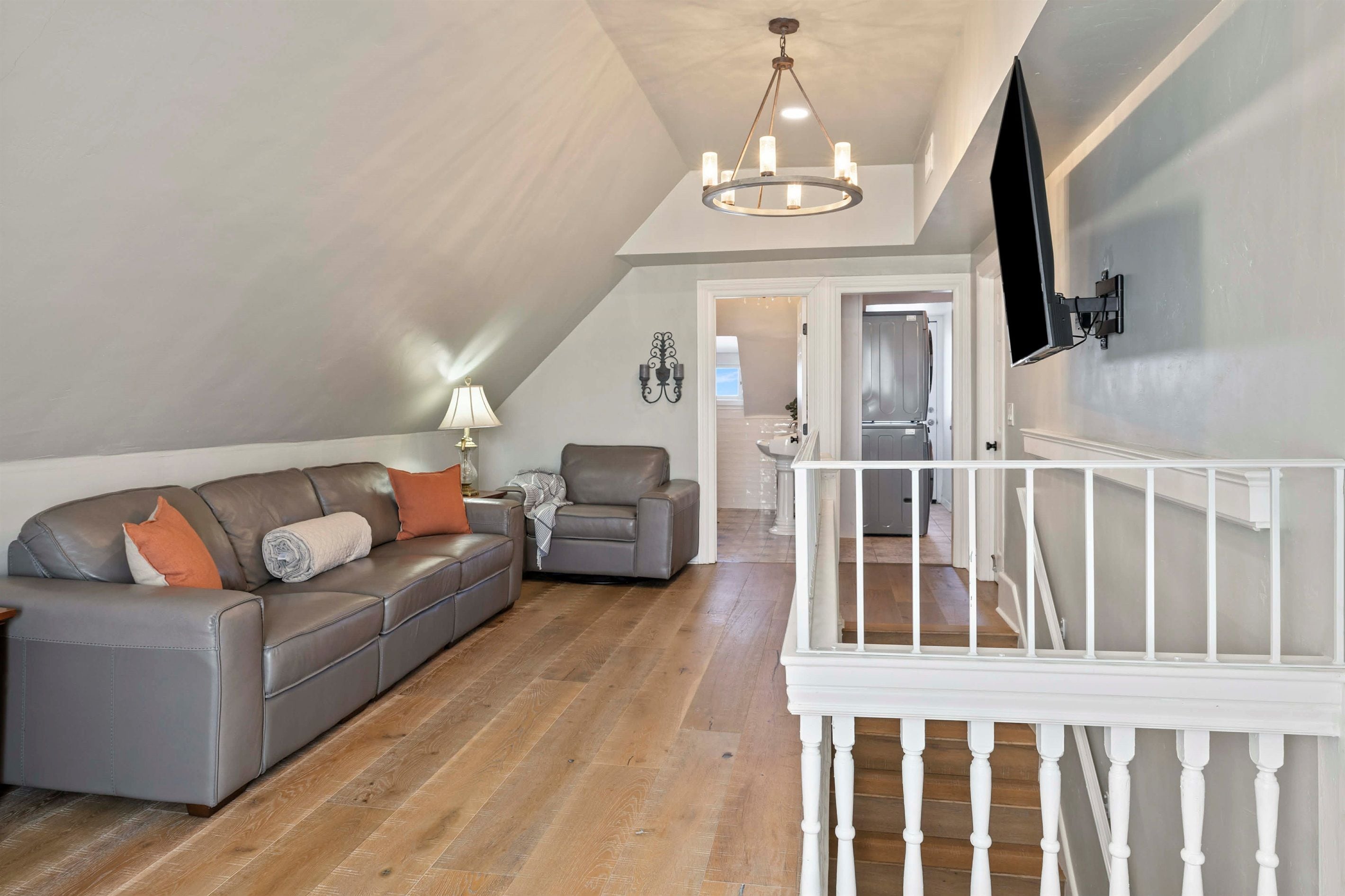 Un vaste salon doté d’un canapé en cuir gris, d’un escalier blanc et d’un téléviseur à écran plat fixé au mur.