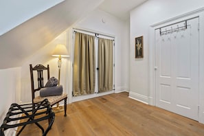 Ein Zimmer mit Holzboden, einem Sessel mit zusammengelegtem Handtuch, einer Lampe, einer Tür mit Garderobe und einem gerahmten Bild an der Wand.