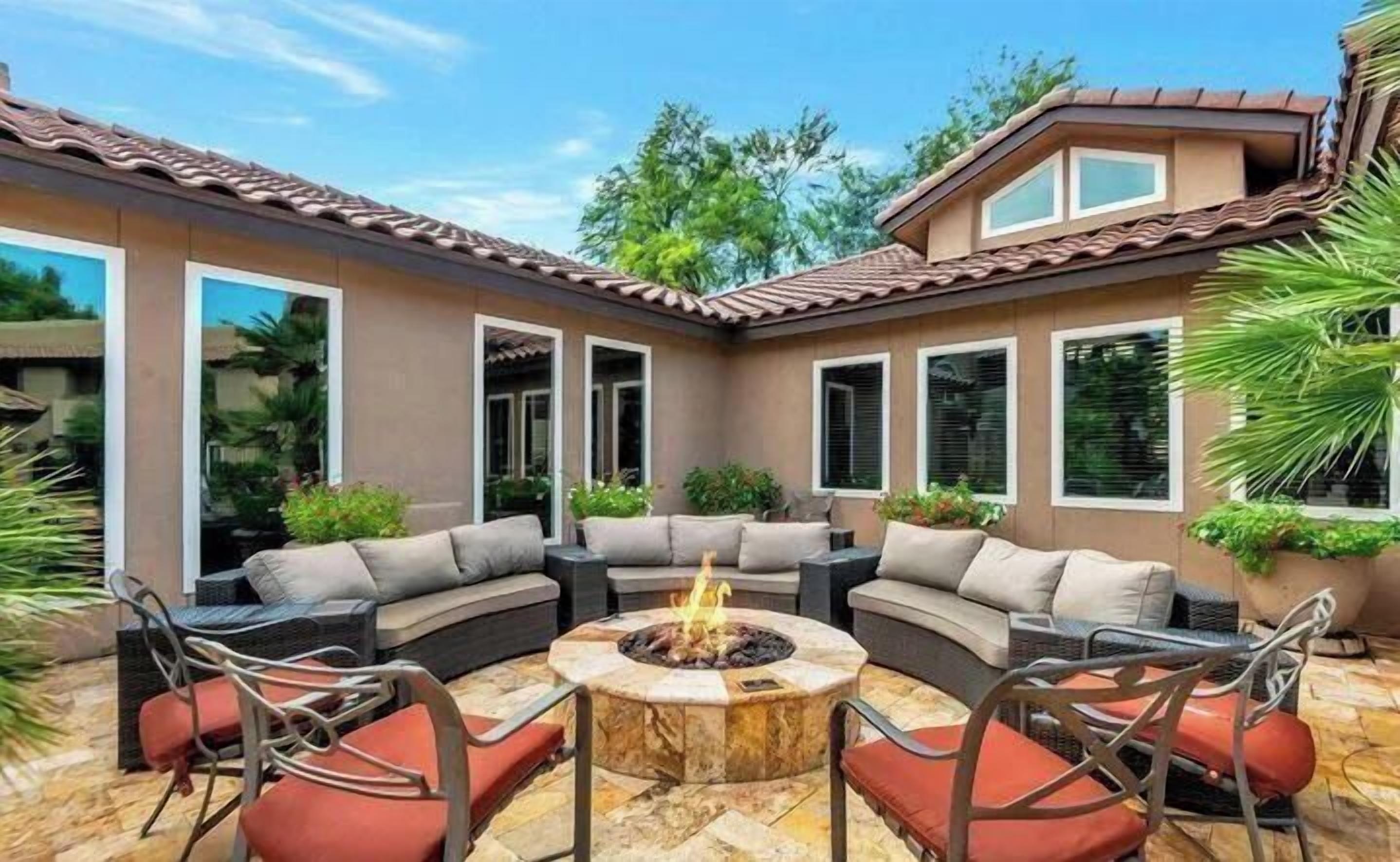 A patio with a circular fire pit, cushioned seating, and potted plants.