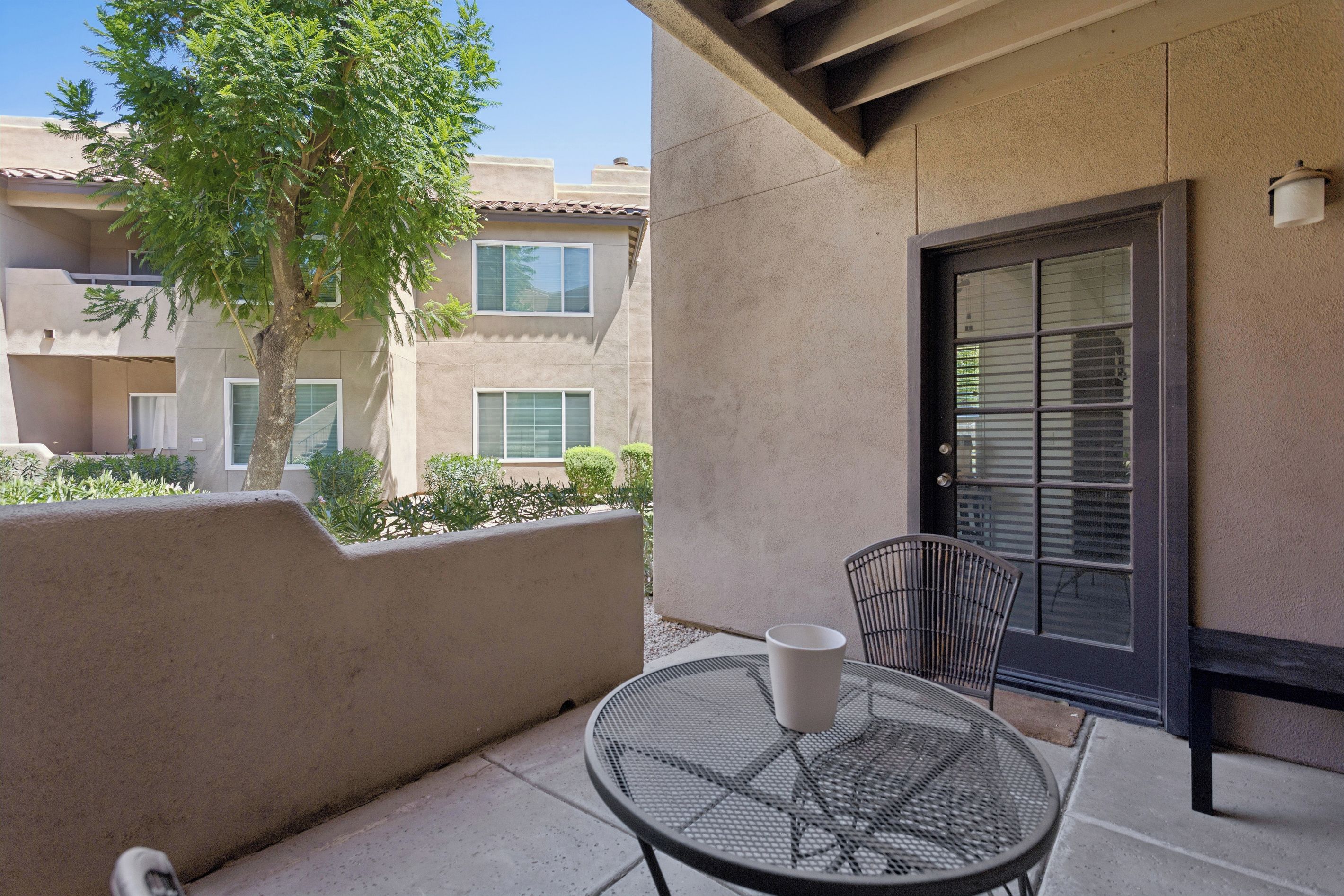 A balcony with a metal table and chairs, a potted plant, and a building in the background.