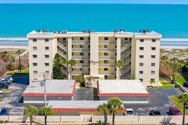 Ein mehrgeschossiges Hotel mit flachem Dach, einem Parkplatz und Blick auf den Strand.