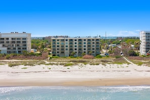 Ein Hotel am Strand mit mehreren Etagen, ein sandiger Strand im Vordergrund und ein klarer, blauer Himmel.