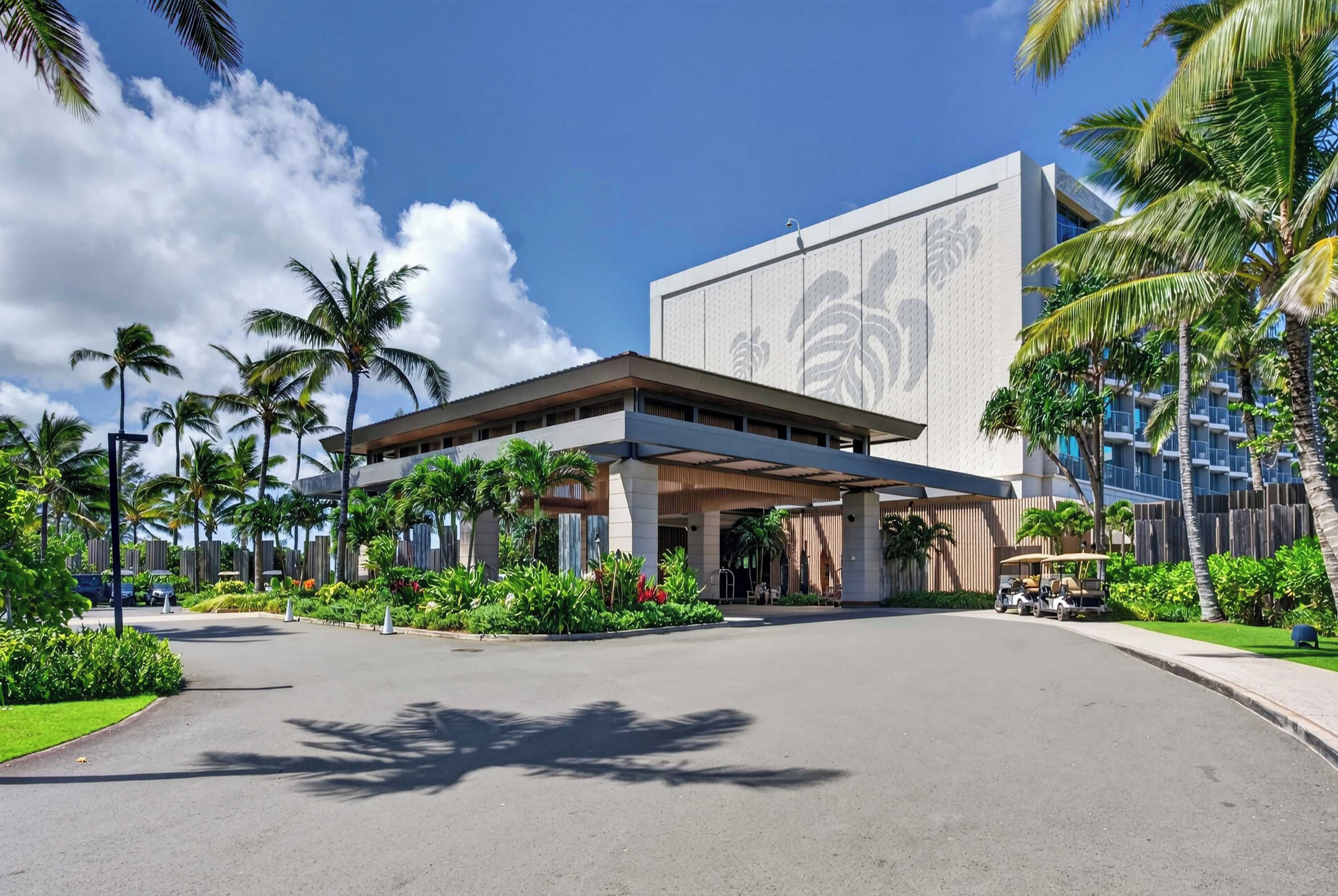 A modern hotel with a covered entrance, palm trees, and a clear sky.