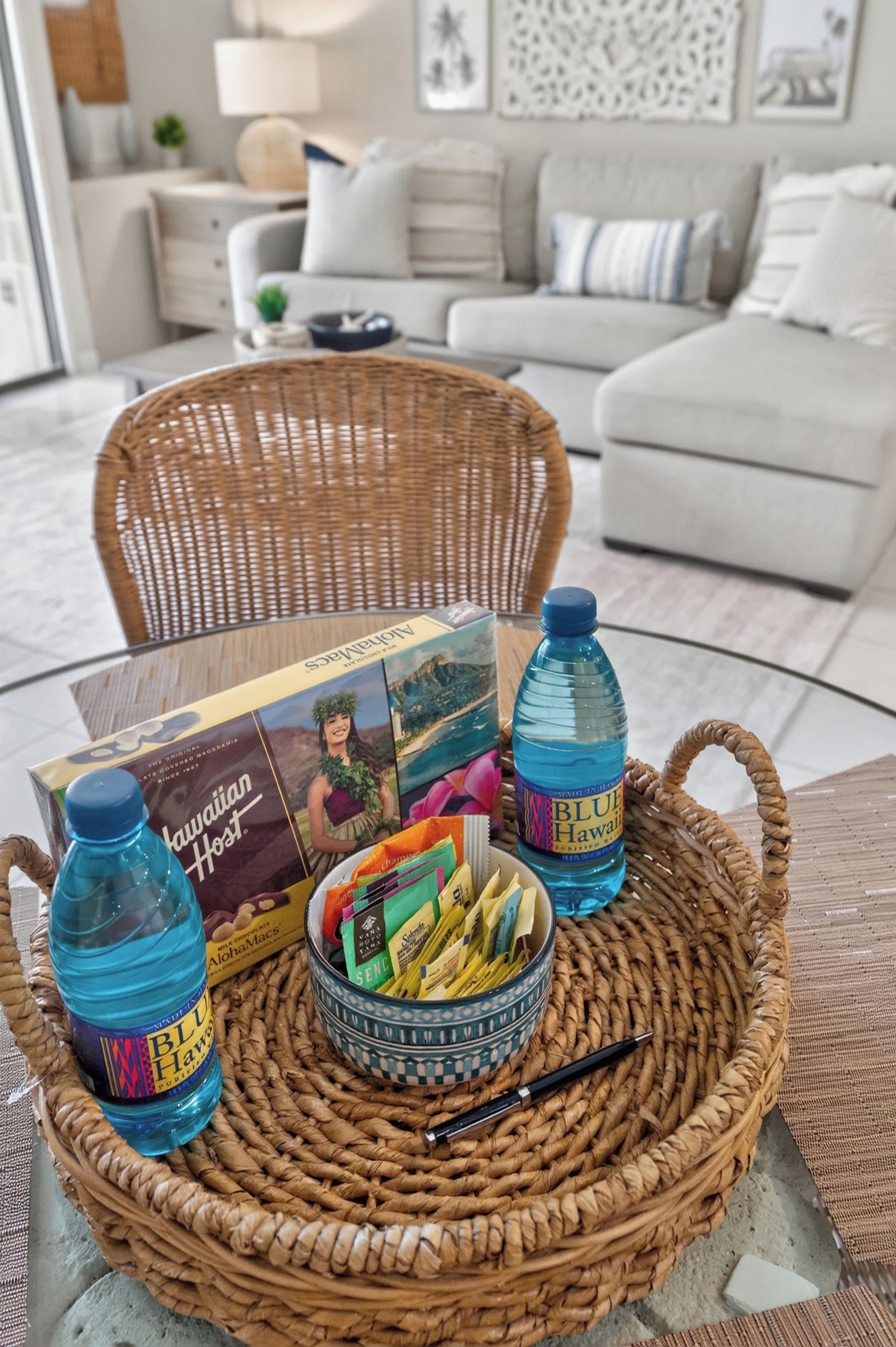 A wicker tray with a box of Hawaiian-themed snacks, two bottles of Blue Hawaii water, and a small bowl of snacks on a table.