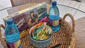 A wicker tray with a box of Hawaiian-themed snacks, two bottles of Blue Hawaii water, and a small bowl of snacks on a table.
