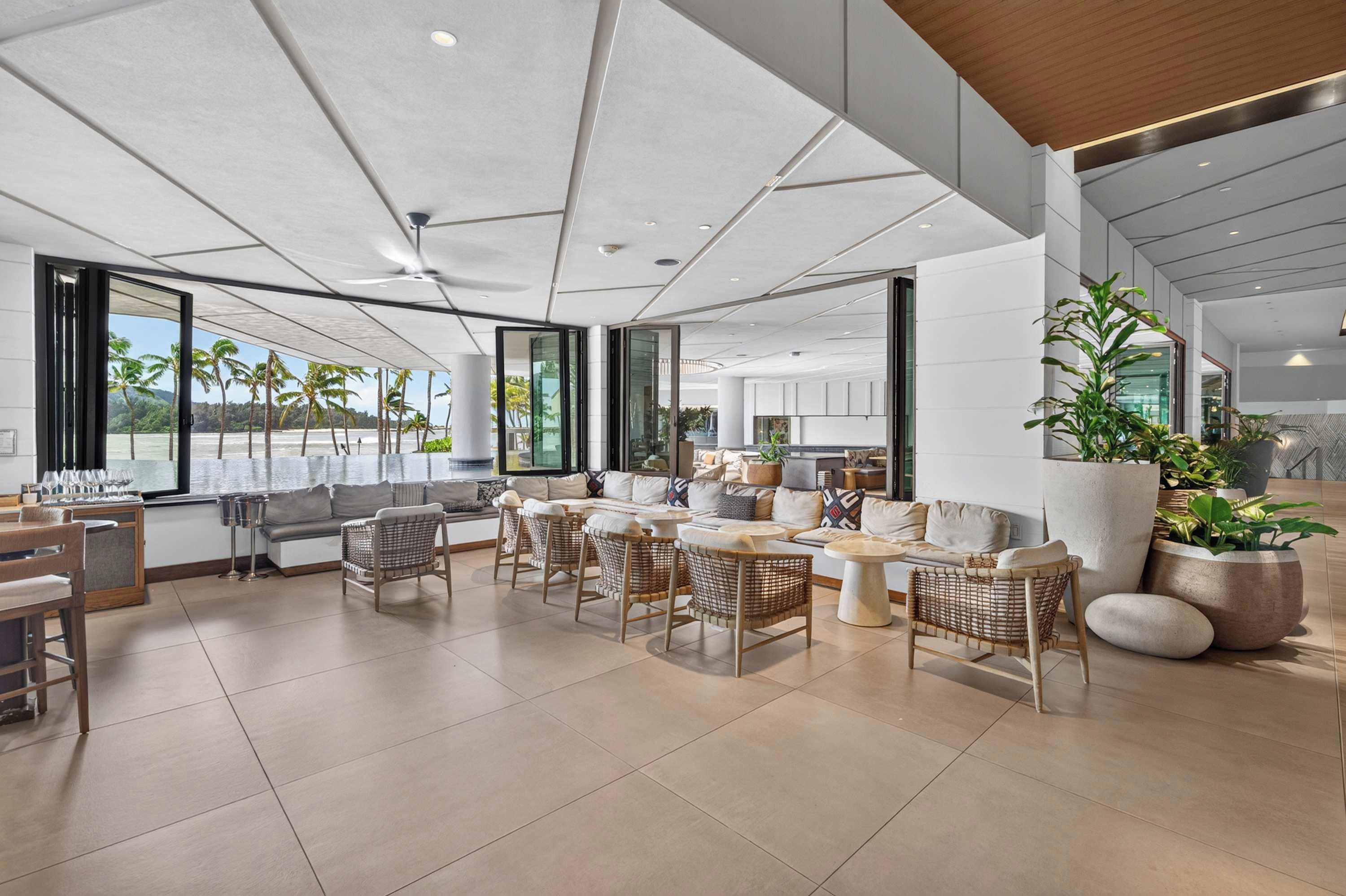 A spacious lounge area with a large window offering a view of palm trees and a beach.