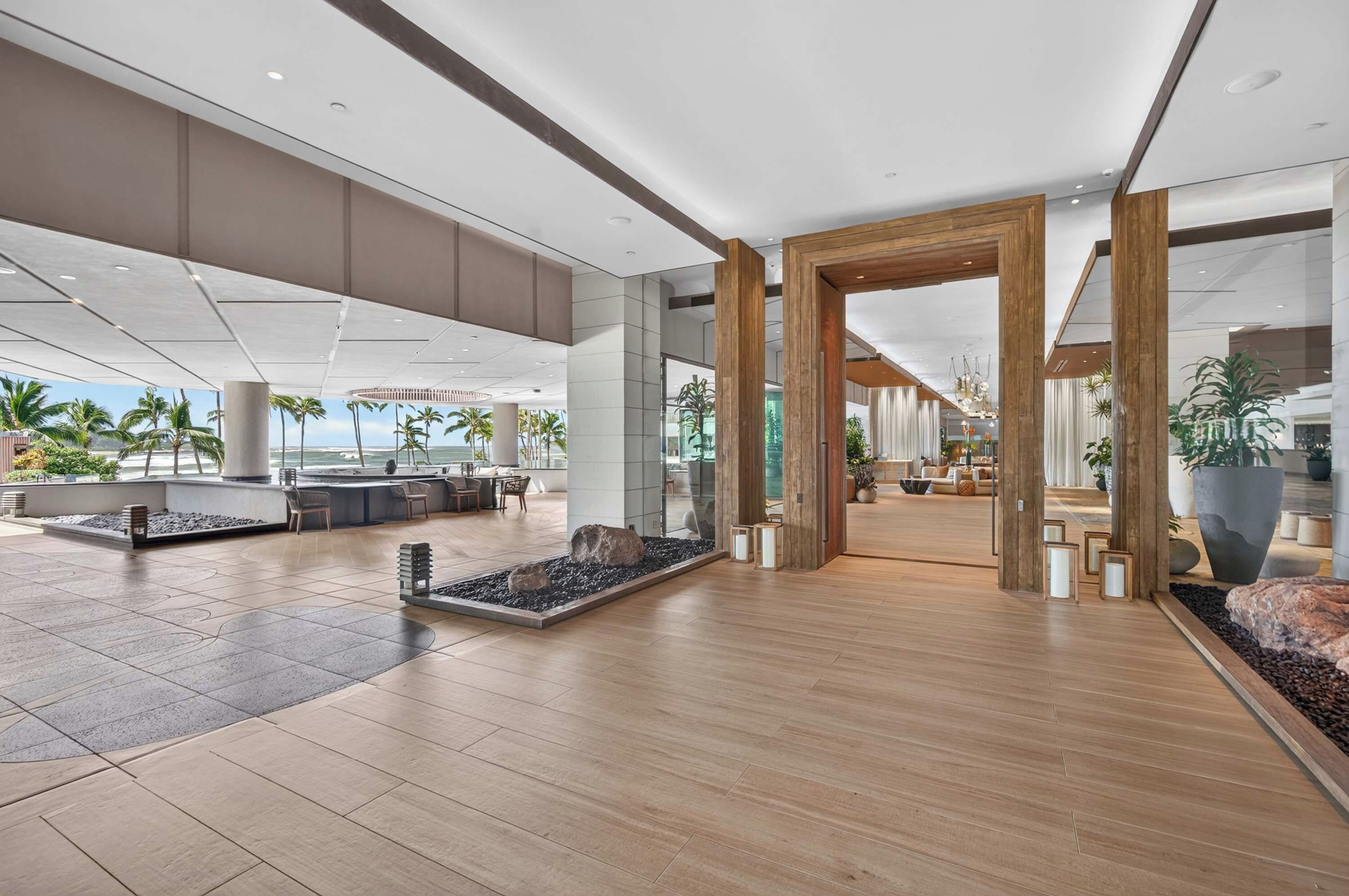 A spacious lobby with a wooden floor, large pillars, and a view of palm trees.