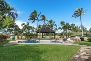 Un área de piscina con un mirador, palmeras y un césped cuidado.