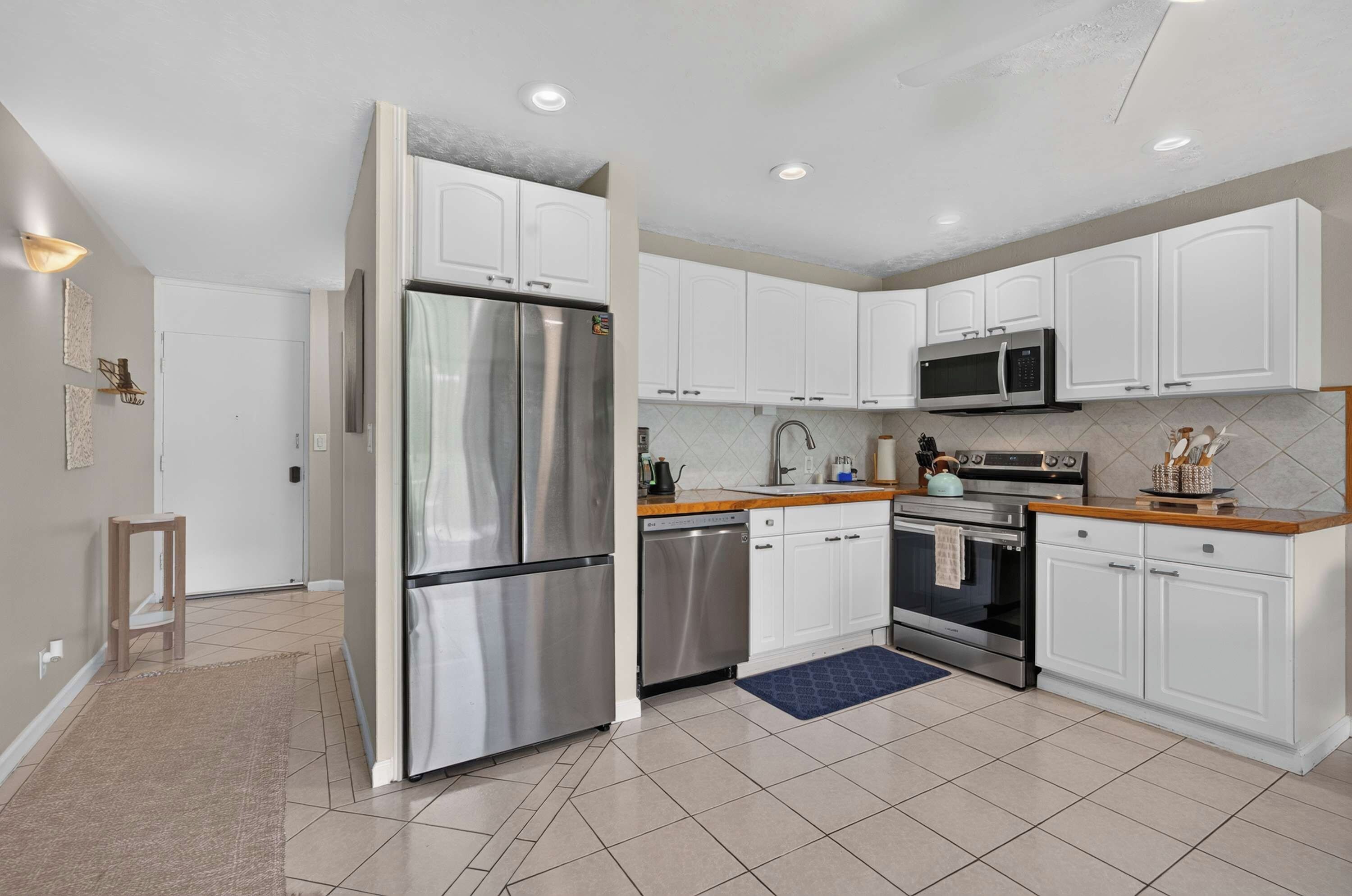 A modern kitchen with stainless steel appliances, white cabinetry, and a tiled floor.
