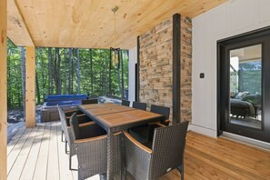Eine Terrasse im Freien mit einem Holztisch, Korbstühlen, einer Steinmauer und Blick auf den Wald.