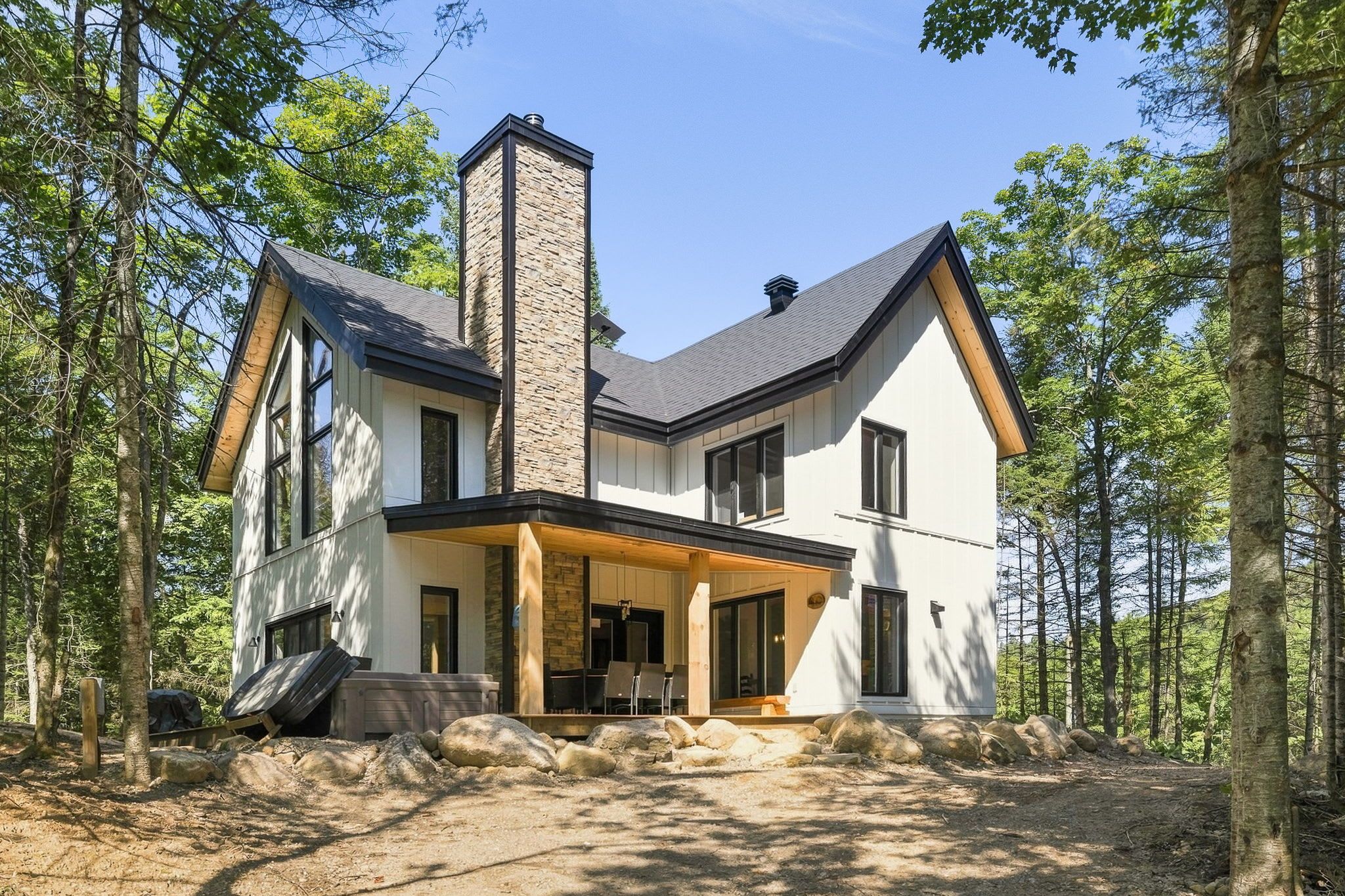 Una casa moderna de dos pisos con chimenea de piedra, ventanas grandes y un porche cubierto.