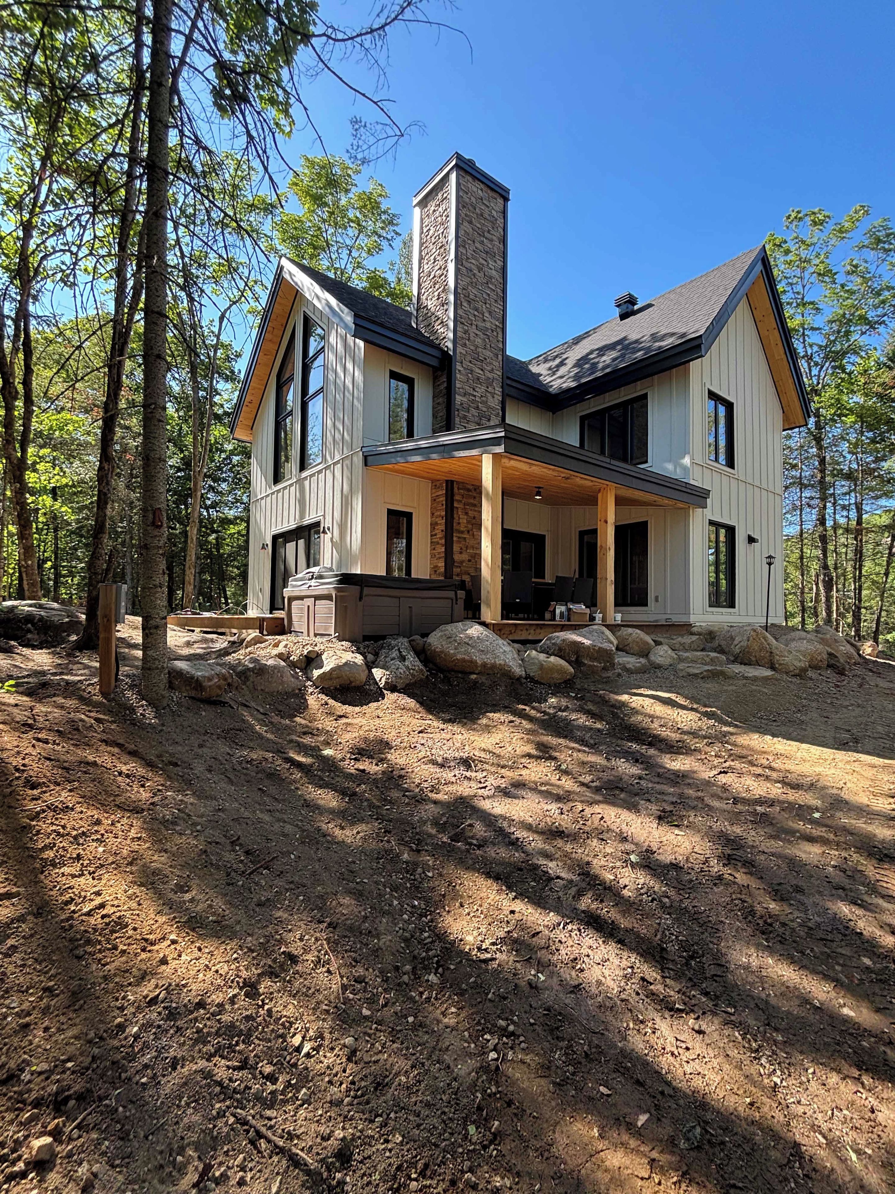 Una casa de dos pisos con chimenea de piedra, ventanas grandes y un porche cubierto.
