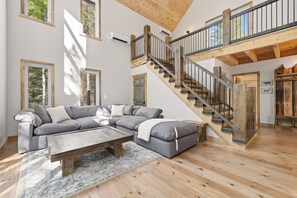 Ein geräumiges Wohnzimmer mit einem großen Ecksofa, einem Holztisch und einer Treppe mit einem Holzapfgel.