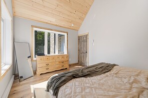 Ein Schlafzimmer mit Holzbalkendecke, einem großen Fenster, einem Schminktisch und einem Bett mit Decke.