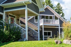 A two-story house with a stone facade, a balcony, and a covered porch. - Two Harbors Contemporary Home, by Heirloom (Two Harbors)