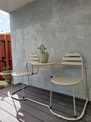Eine Terrasse mit zwei Metallstühlen, einem Tisch, einem Blumentopf und einer Betonmauer.
