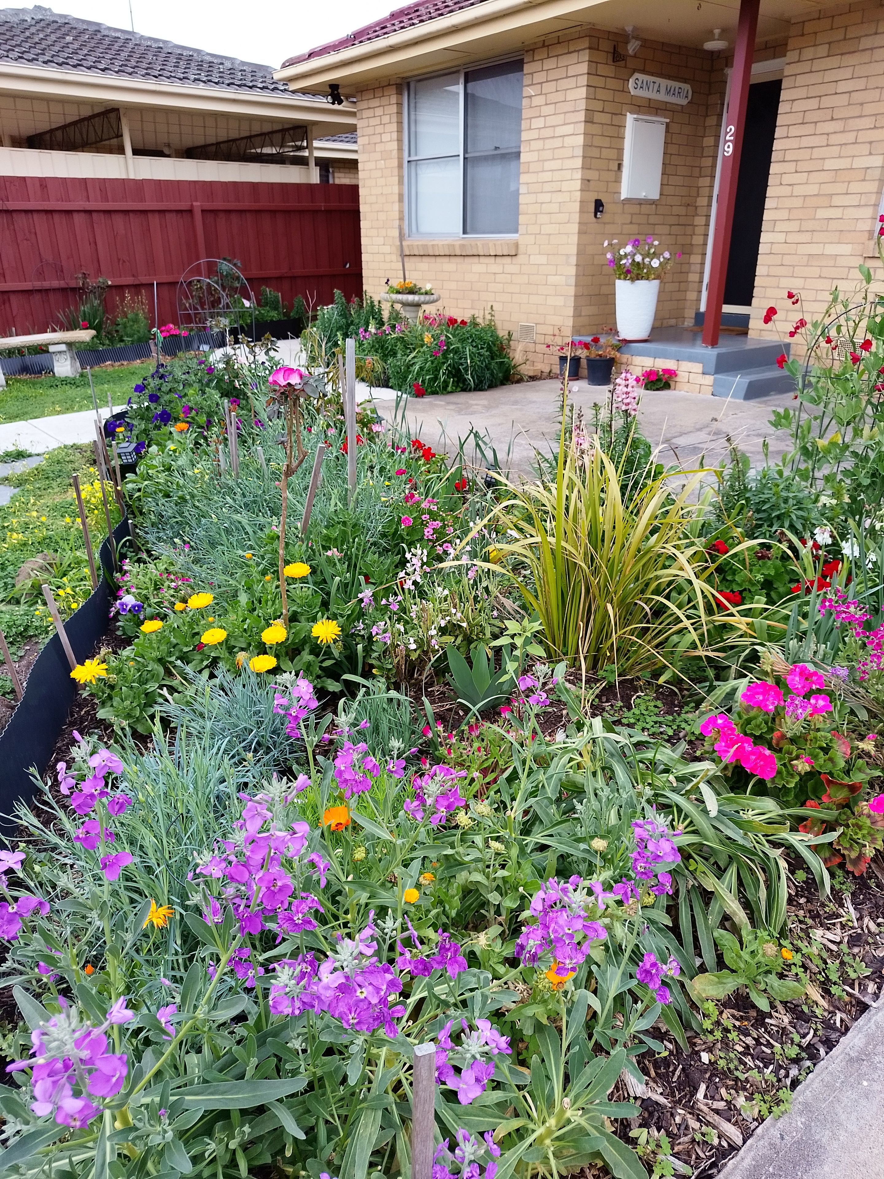 Een woonhuis met een bakstenen gevel, een voortuin met verschillende bloeiende planten en een brievenbus.
