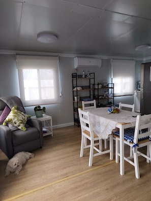 Ein Wohnzimmer mit einer Couch, einem Esstisch mit Stühlen, einem kleinen weißen Tisch und einem Blumentopf.