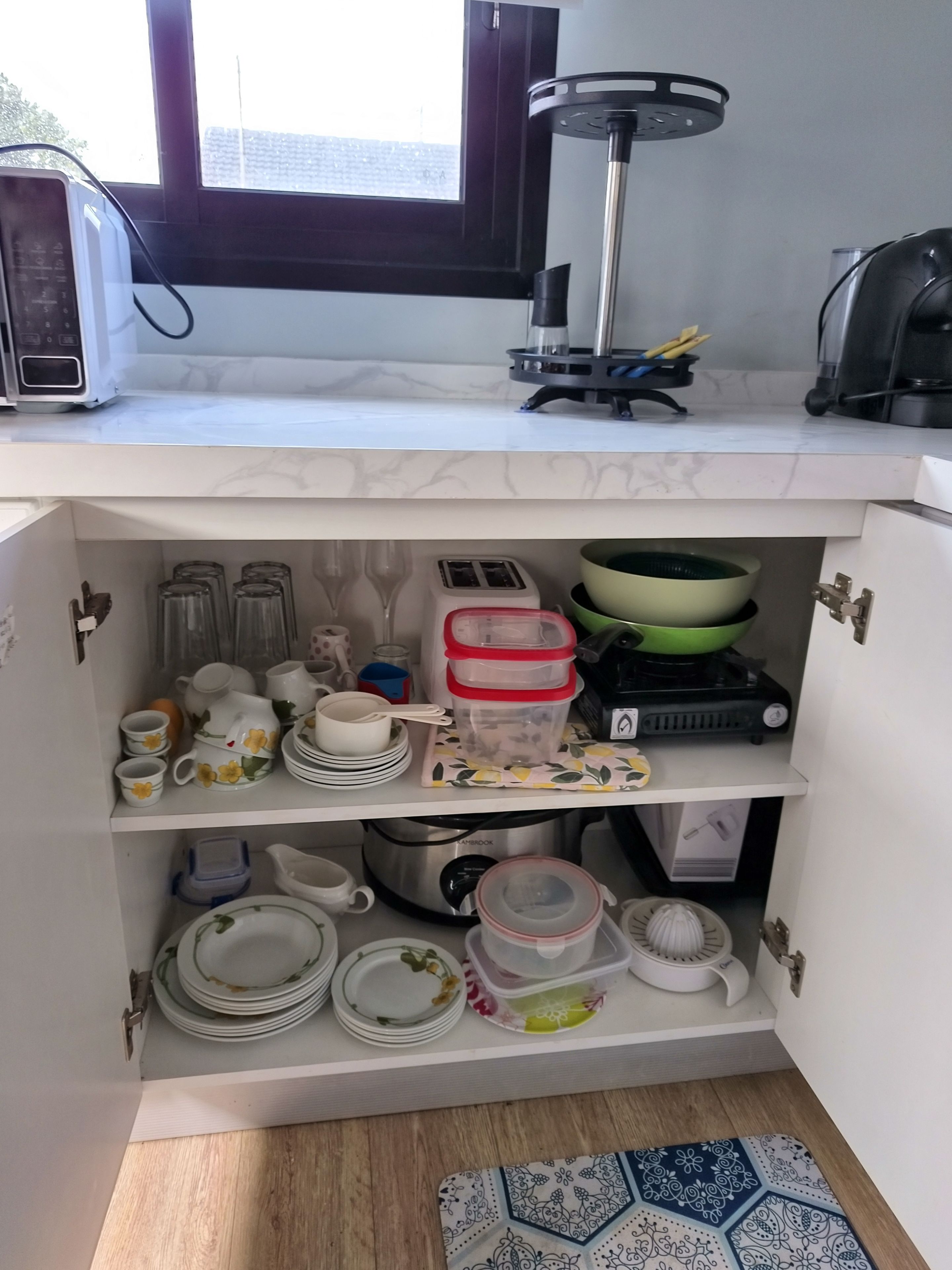 A kitchen with a microwave, toaster, and kettle on the countertop. There are shelves below with various dishes and containers.