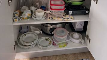 A kitchen with a microwave, toaster, and kettle on the countertop. There are shelves below with various dishes and containers.
