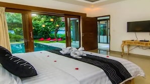 A hotel room with a bed, a desk, a TV, and a view of a pool and greenery. - Cozzy Fullmoon Purnama Villa Ubud (Gianyar)