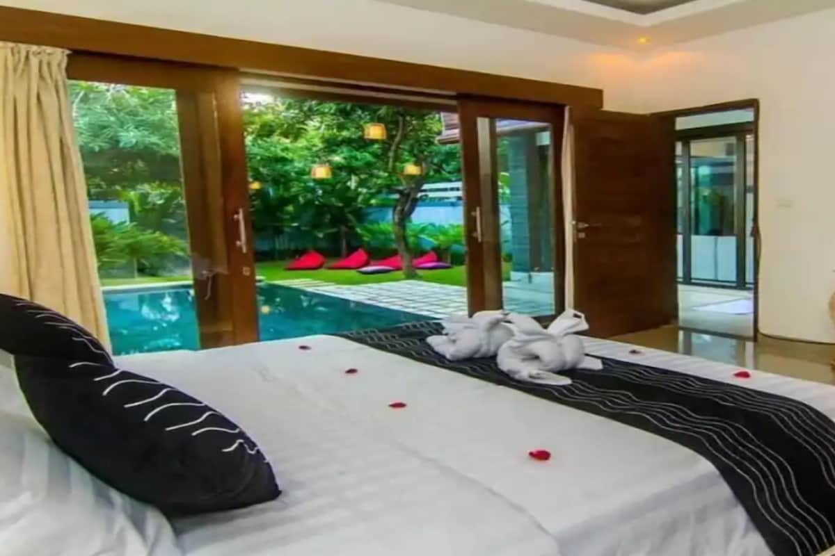 A hotel room with a bed, a desk, a TV, and a view of a pool and greenery.