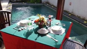 A dining table set with plates, cutlery, and a flower centerpiece, overlooking a swimming pool. - Cozzy Fullmoon Purnama Villa Ubud (Gianyar)