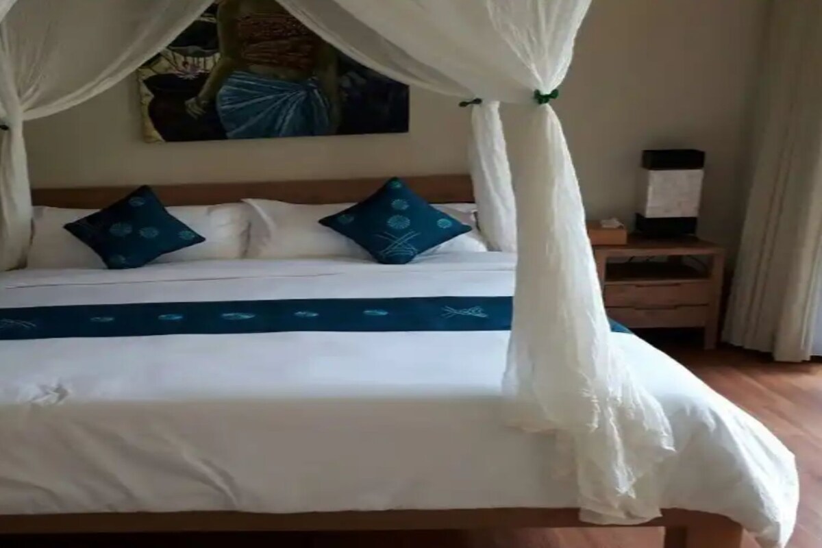 A bed with a canopy, two pillows, a nightstand, and a painting on the wall.