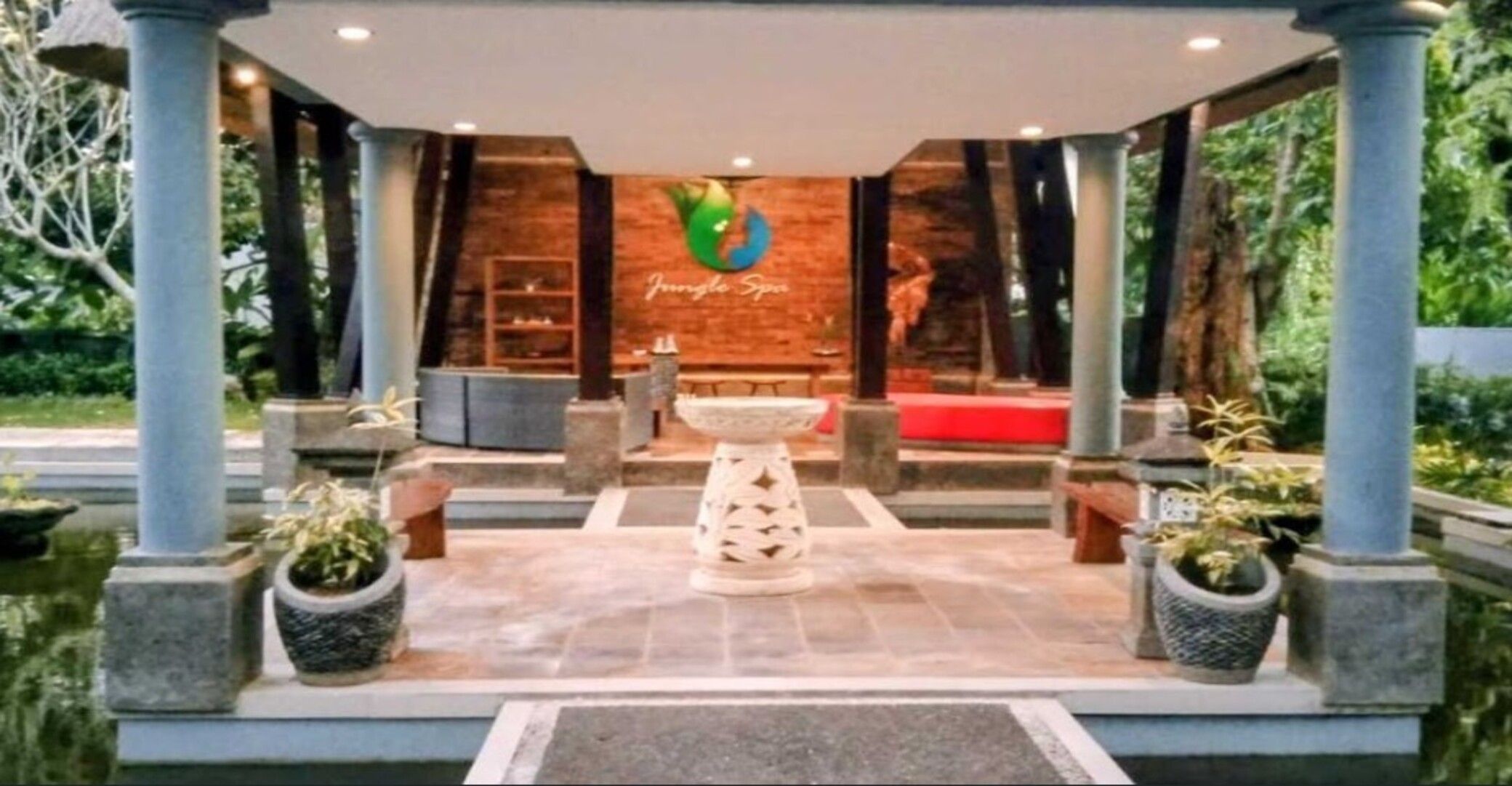 A reception area with a central water feature, a seating area, and a brick wall with a logo.