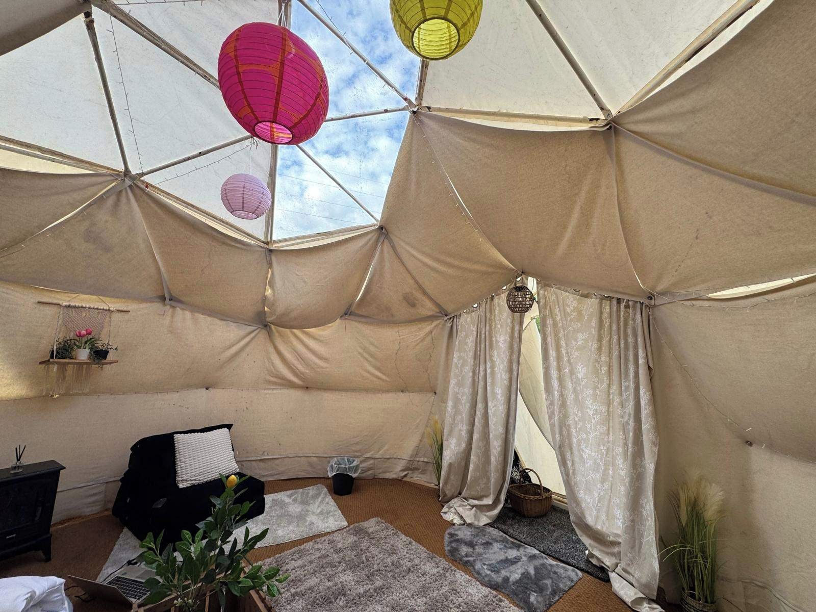 Een tent met een geometrisch plafondontwerp, een bed, een bureau en een potplant.