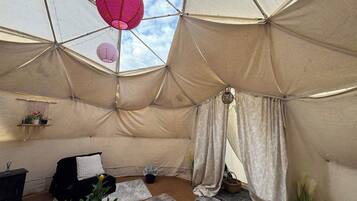 Een tent met een geometrisch plafondontwerp, een bed, een bureau en een potplant.