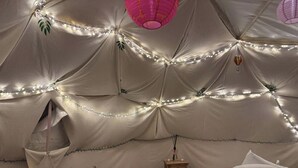 A tent-like room with string lights, a lantern, a small wooden table, and a bed with pillows. - The Leaf & Lantern Dome - Sleeps 5 - Dog Friendly (Pewsey)