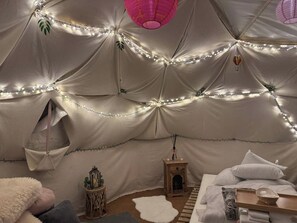 Una habitació semblant a una tenda, amb llums penjades, un fanal, una taula de fusta petita i un llit amb almoades.