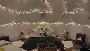 A cozy tent-style room with a bed, a small table with a plant, a heater, and string lights. - The Leaf & Lantern Dome - Sleeps 5 - Dog Friendly (Pewsey)