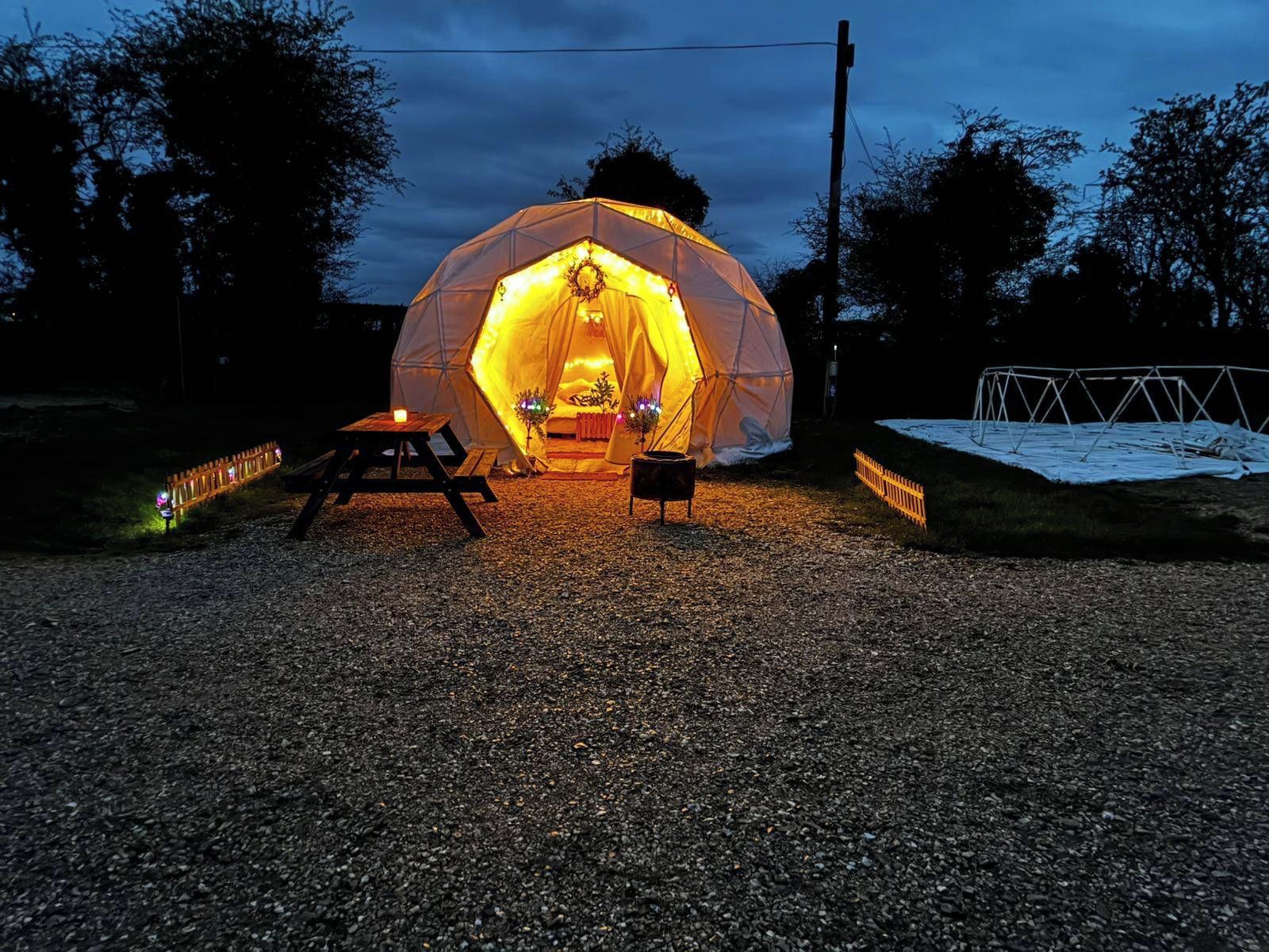 A geodesic dome tent with a table and chairs outside at dusk.