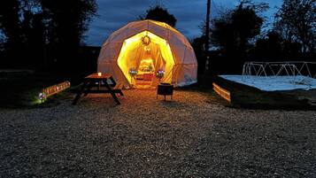 A geodesic dome tent with a table and chairs outside at dusk.