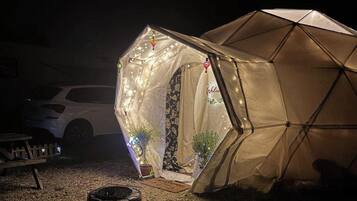 Een tent met een luifel en lichtjes, een geparkeerde auto in de buurt, en een klein tafeltje met spullen erop.