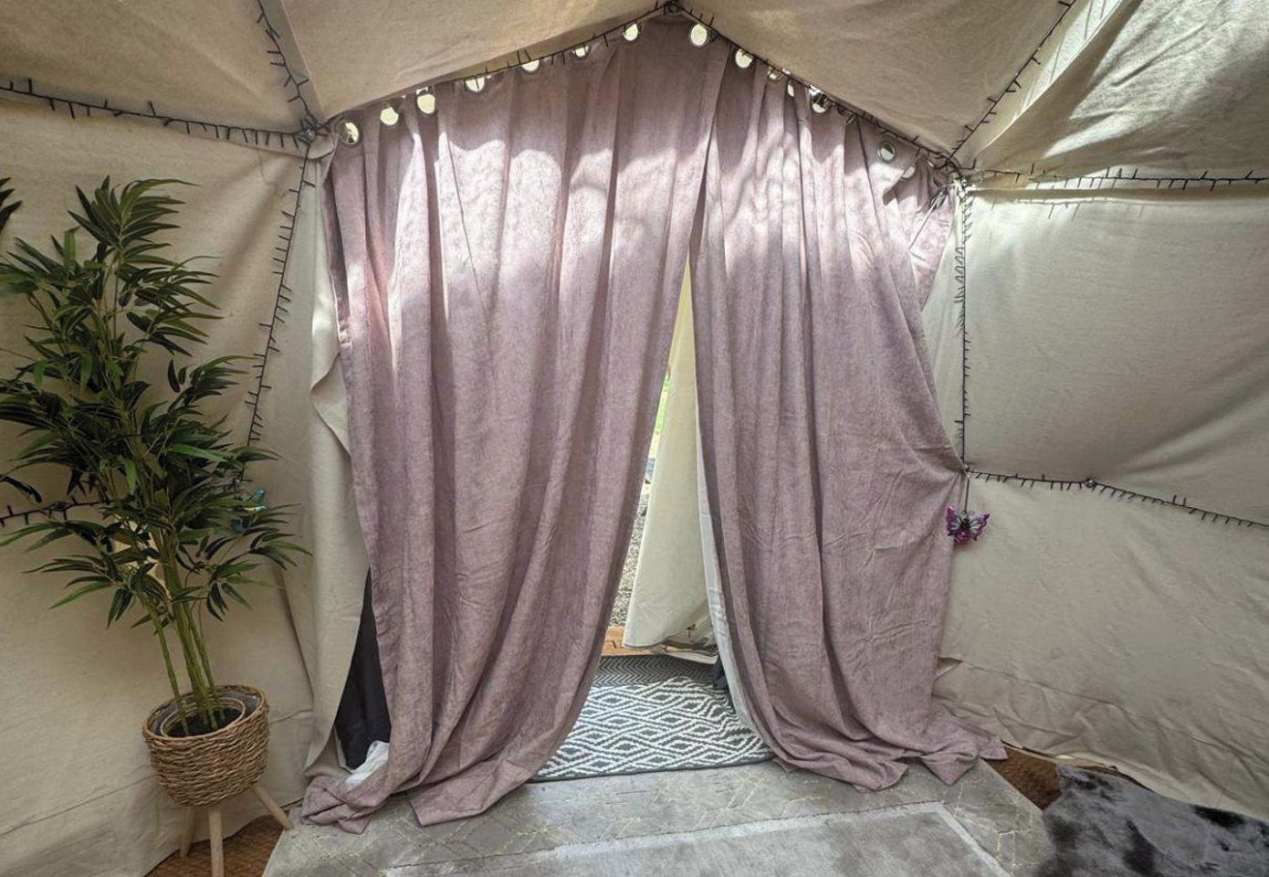 A tent with a woven plant stand, a patterned rug, and a door with a curtain.