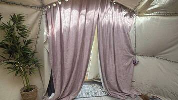 A tent with a woven plant stand, a patterned rug, and a door with a curtain.